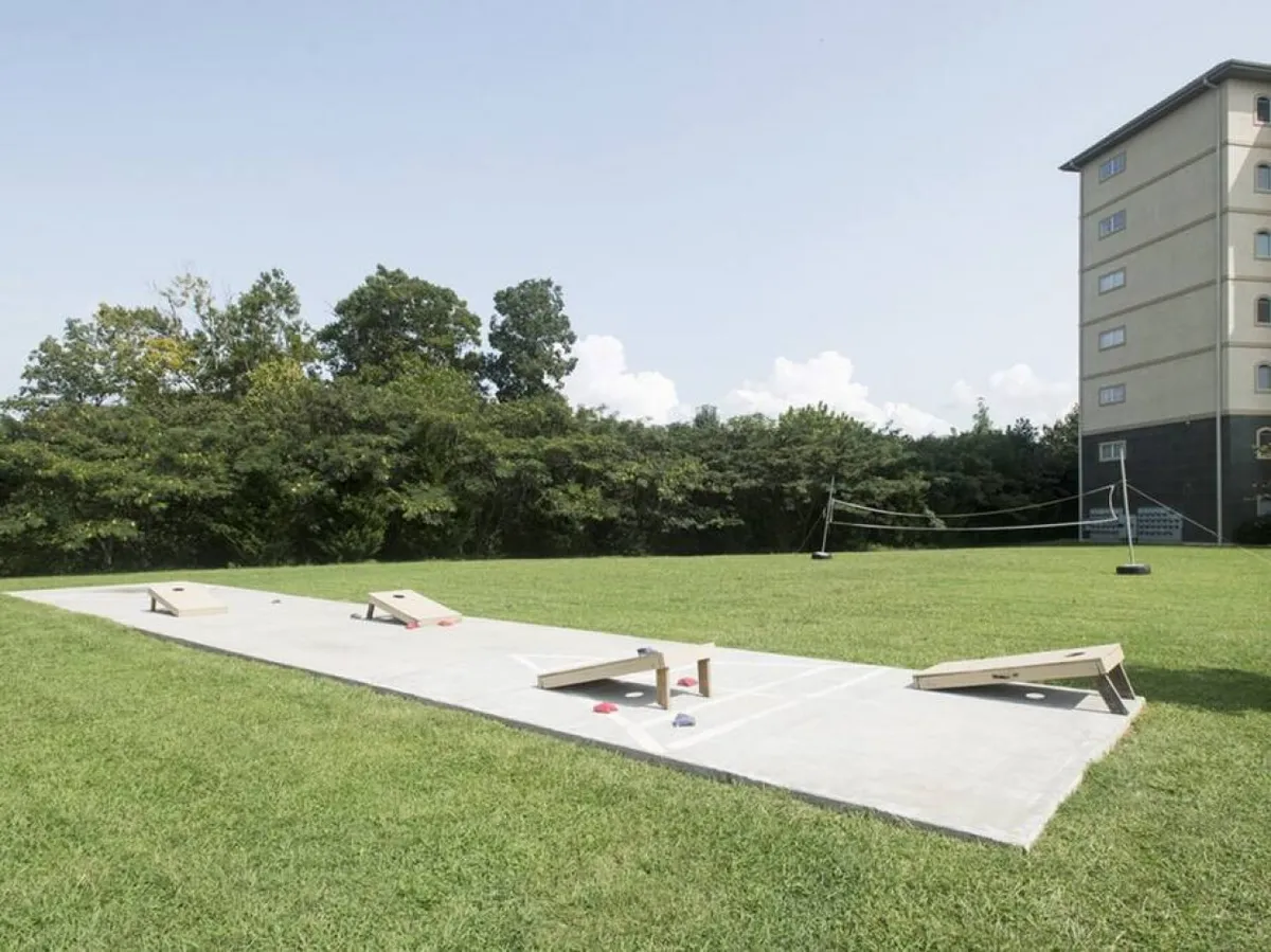 An outdoor bean bag toss (cornhole) area with green grass, surrounded by trees and a building in the background, inviting guests to enjoy games and gatherings.