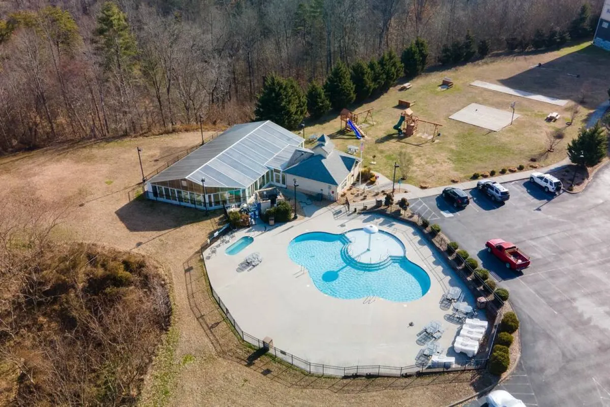 This exterior image captures a vibrant recreation area featuring a swimming pool, a playground, and plenty of open space, all set against a backdrop of greenery. The scene clearly shows children’s play structures and lounging areas, suggesting a lively, family-friendly atmosphere.