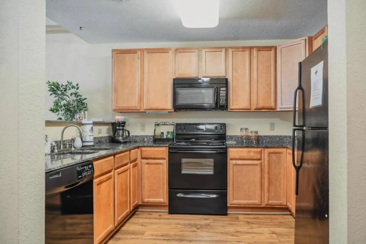 A view of a kitchen featuring black modern appliances, granite countertops, and wooden cabinets. The kitchen sink is visible, and the layout suggests ample workspace for meal prep and cooking. The lighting feels warm and inviting, emphasizing the functionality of the kitchen.