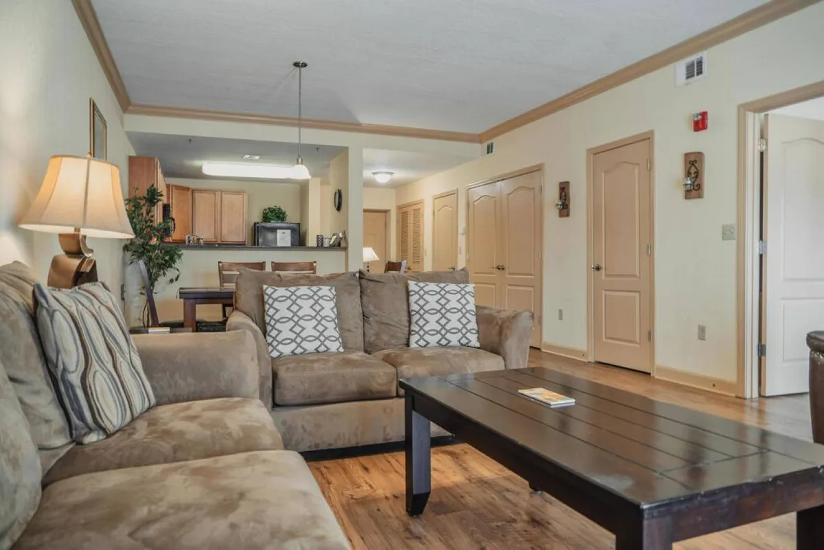 A comfortable living space with a large couch, wooden coffee table, and a kitchen area in the background. The scene is styled for relaxing, entertaining guests, and enjoying family time, with warm lighting and homely touches.