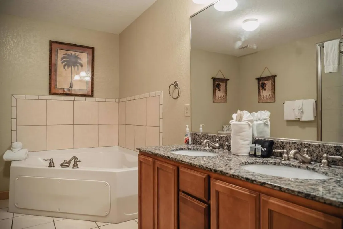 A serene bathroom with a large, inviting bathtub, dual vanities, framed artwork, and fresh towels. The mood is tranquil and spa-like, perfect for unwinding after a day of exploration, with plenty of space and accessible amenities.