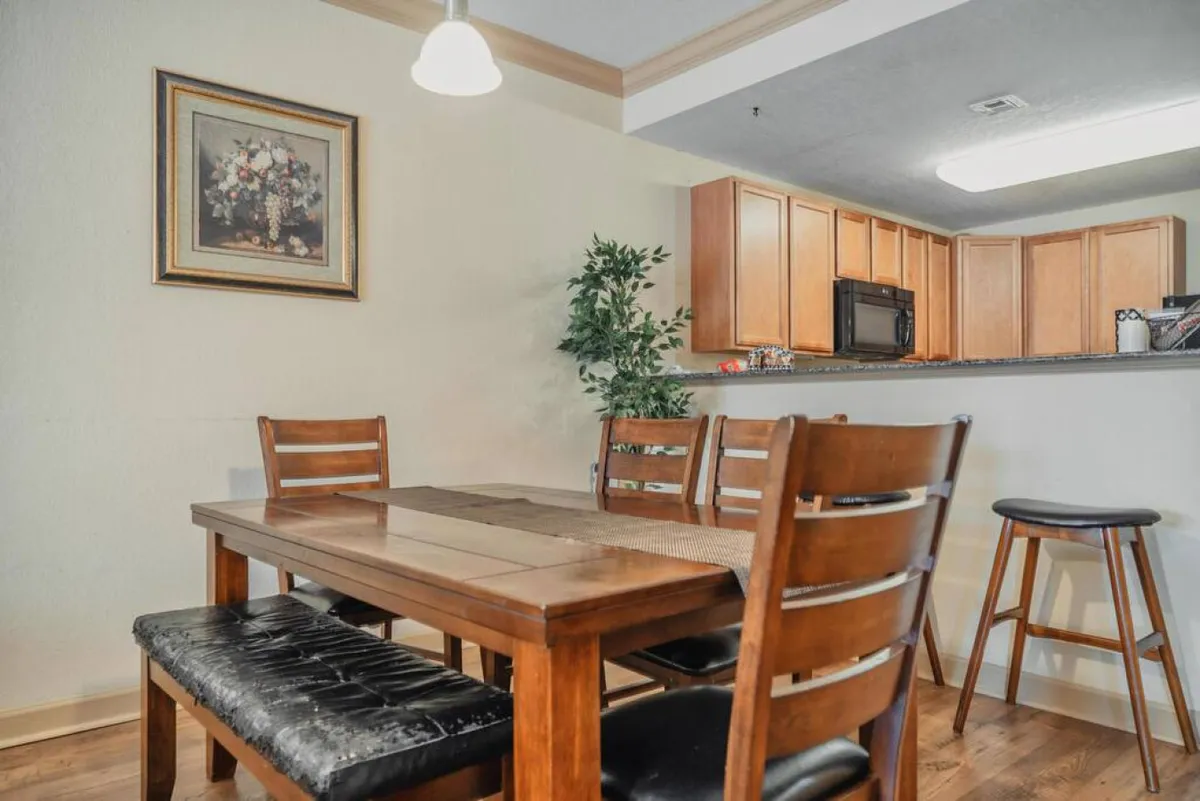 A view of the dining table and kitchen area, with decorative artwork and an indoor plant visible. The layout is open and warm, encouraging casual dining and conversation. The atmosphere is welcoming and homely.