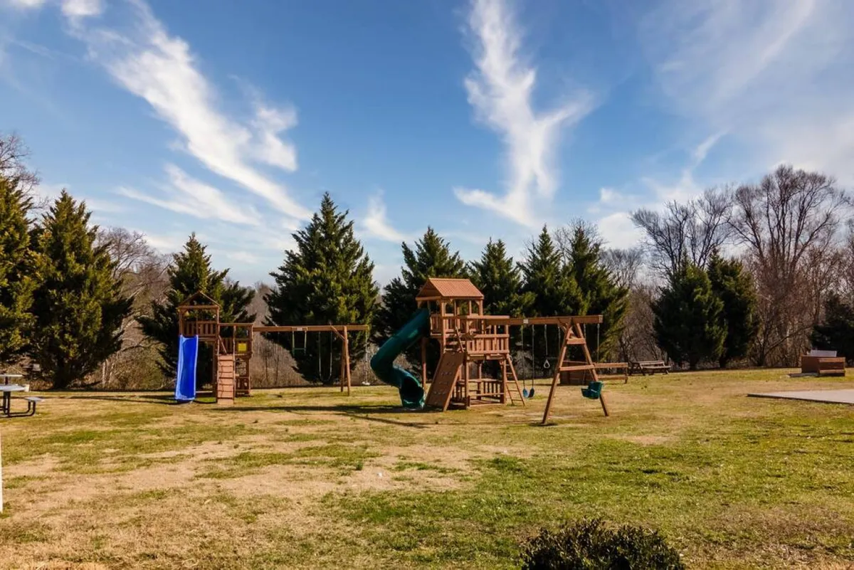 A vibrant playground structure with swings and a slide, set among tall trees, where children enjoy outdoor play while families gather nearby.