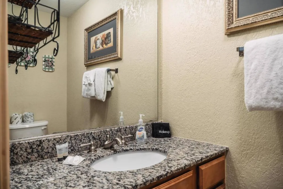 An inviting bathroom vanity with a granite countertop, large mirror, framed artwork, sink, and neatly arranged towels. The organized, cozy setting is perfect for morning routines or winding down in the evening.