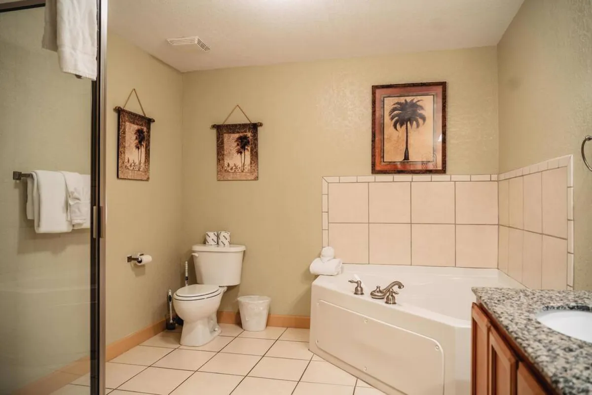 A tranquil bathroom featuring a garden-style soaking bathtub, granite countertop, framed palm tree artwork, and neatly arranged towels. The scene exudes a spa-like, peaceful atmosphere perfect for self-care and relaxation.